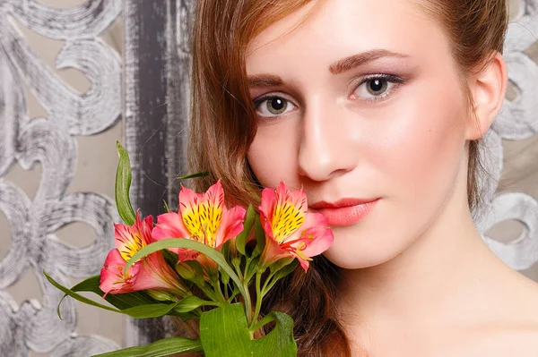 Young beautiful lady with flowers on grey background. Skin care concept. Portrait of a young sweet girl in the studio on a gray background with a green flower in hand