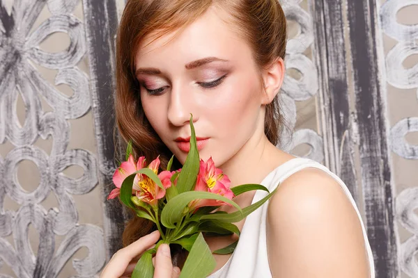 Young beautiful lady with flowers on grey background. Skin care concept. Portrait of a young sweet girl in the studio on a gray background with a green flower in hand