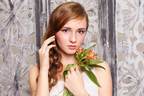 Young beautiful lady with flowers on grey background. Skin care concept. Portrait of a young sweet girl in the studio on a gray background with a green flower in hand