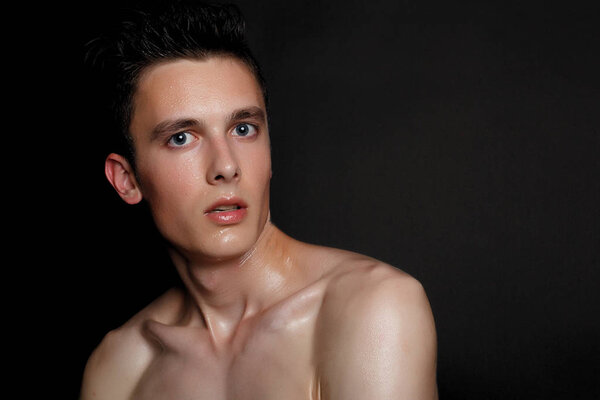 Handsome young man isolated. Beauty portrait of shirtless muscular man is standing on black background and looking at camera. Men's health.