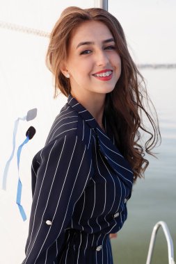 Çekici kız yaz gününde bir yatta. Yat poz çarpıcı romantik kadın moda portresi kapatın. Bir zarif elbise, yaz kıyafeti giyiyor. Mavi gökyüzü. günbatımı