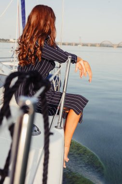 Çekici kız yaz gününde bir yatta. Yat poz çarpıcı romantik kadın moda portresi kapatın. Bir zarif elbise, yaz kıyafeti giyiyor. Mavi gökyüzü. günbatımı