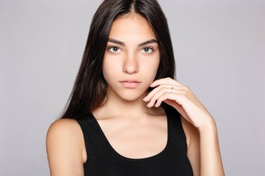 Gülümseyen bir çekici kameraya bakarak portre. Siyah elbise giymiş. Gri arka plan üzerinde poz. Temiz cilt, doğal makyaj ve beyaz dişler ile gülümseyen güzel kadın