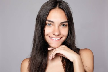 Gülümseyen bir çekici kameraya bakarak portre. Siyah elbise giymiş. Gri arka plan üzerinde poz. Temiz cilt, doğal makyaj ve beyaz dişler ile gülümseyen güzel kadın