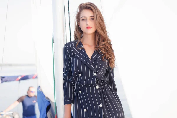 Attractive girl on a yacht at summer day. Close up of fashion portrait of stunning romantic woman posing yacht. Wearing an elegant dress, summer outfit. Blue sky. sunset