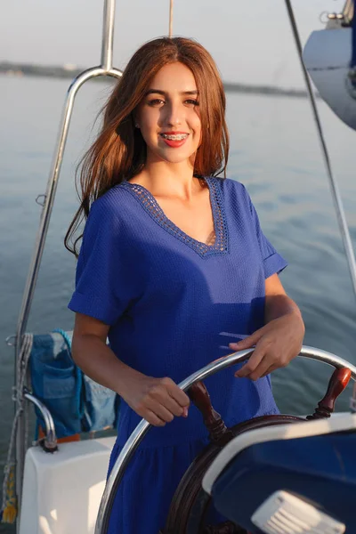 Attractive girl on a yacht at summer day. Close up of fashion portrait of stunning romantic woman posing yacht. Wearing an elegant dress, summer outfit. Blue sky. sunset