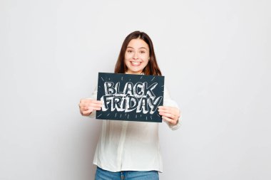 Alışveriş, perakende, siyah Cuma, satış, alışveriş ve insanlar kavramı - genç gülümseyen esmer kız siyah Cuma işareti tutuyor. Siyah Cuma satış.