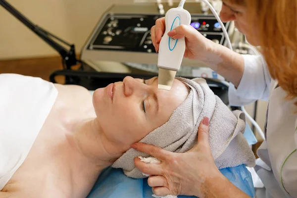 people, beauty, spa, cosmetology and technology concept - The cosmetologist makes the procedure ultrasonic face peeling of the facial skin of a beautiful, young woman in a beauty salon