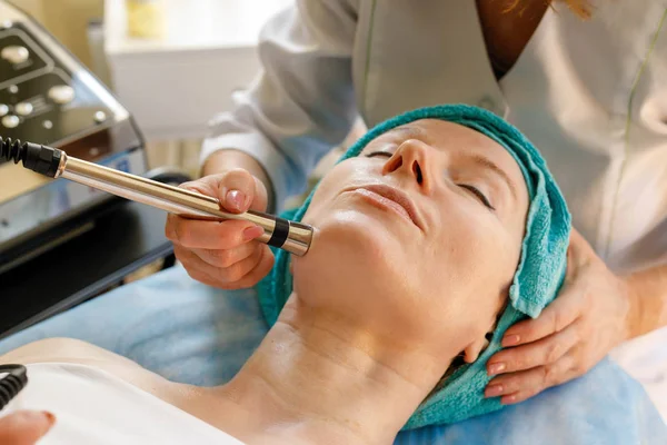 people, beauty, spa, cosmetology and technology concept - Cosmetologist makes the procedure microcurrent therapy of the facial skin of a beautiful, young woman in a beauty salon