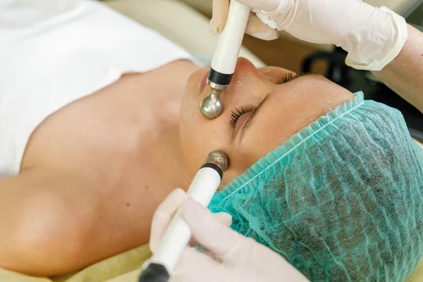 people, beauty, spa, cosmetology and technology concept - Cosmetologist makes the procedure microcurrent therapy of the facial skin of a beautiful, young woman in a beauty salon
