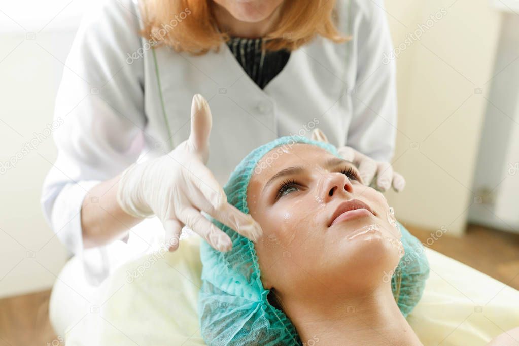 people, beauty, spa, cosmetology and technology concept - The cosmetologist makes the procedure ultrasonic face peeling of the facial skin of a beautiful, young woman in a beauty salon