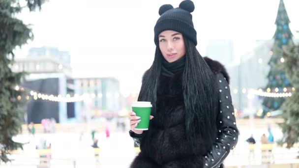 热饮和人的概念 女孩在城市里的一个冬天的早晨在户外喝热咖啡 背景上的溜冰场 人们滑冰 — 图库视频影像