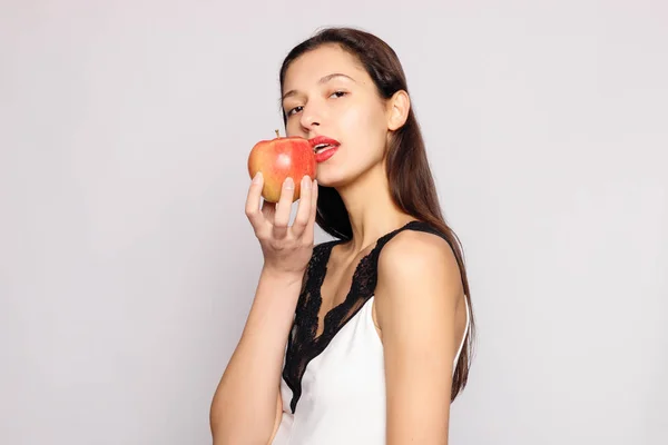 Healthy eating. Woman biting red apple with perfect teeth over grey background