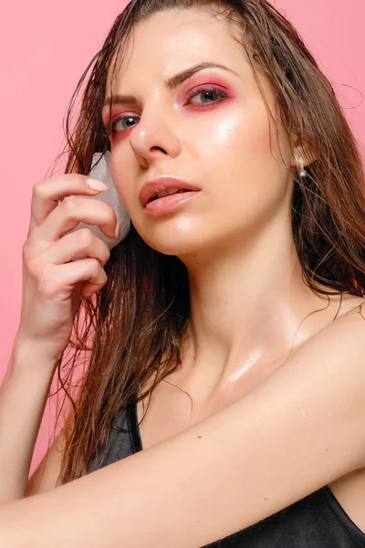 Jovem mulher aplica o gelo ao rosto em um fundo rosa . — Fotografia de Stock