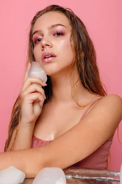 Mujer joven aplica el hielo a la cara sobre un fondo rosa . —  Fotos de Stock