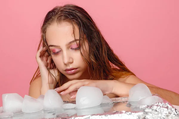 Mladá žena použije ledu čelit na růžovém pozadí. — Stock fotografie