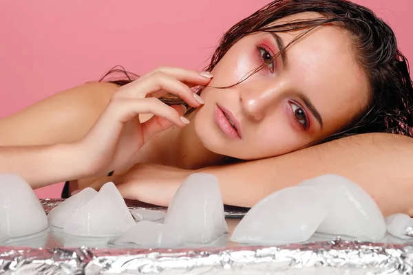Młoda kobieta ma zastosowanie lodu do twarzy na różowym tle. — Zdjęcie stockowe