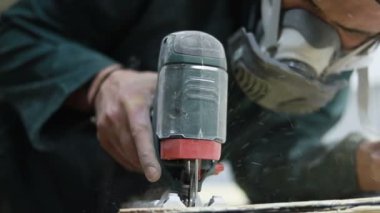 Meslek, insanlar, marangozluk, duygu ve insanlar kavramı-bir marangoz bir elektrikli jigsaw ile bir tahta keser. pateboardlar imalatı. Koruyucu Giyim ve maske vardır. 4k