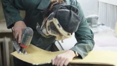 Meslek, insanlar, marangozluk, duygu ve insanlar kavramı-bir marangoz bir elektrikli jigsaw ile bir tahta keser. pateboardlar imalatı. Koruyucu Giyim ve maske vardır. 4k