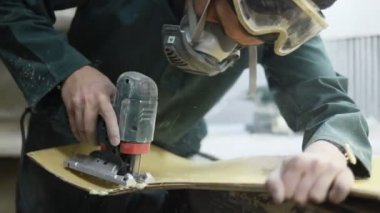 Meslek, insanlar, marangozluk, duygu ve insanlar kavramı-bir marangoz bir elektrikli jigsaw ile bir tahta keser. pateboardlar imalatı. Koruyucu Giyim ve maske vardır. 4k