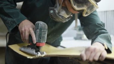 Meslek, insanlar, marangozluk, duygu ve insanlar kavramı-bir marangoz bir elektrikli jigsaw ile bir tahta keser. pateboardlar imalatı. Koruyucu Giyim ve maske vardır. 4k