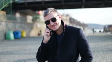 Genç yakışıklı işadamı cadde boyunca geri telefon yürüyüş İş görüşmesinde şık erkek takım elbise görünümüdür konuşuyor, cityscape arka plan üzerinde duruyor. Konsept: teknoloji, iş.