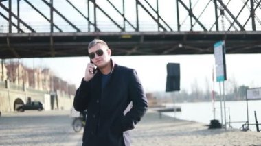 Genç yakışıklı işadamı cadde boyunca geri telefon yürüyüş İş görüşmesinde şık erkek takım elbise görünümüdür konuşuyor, cityscape arka plan üzerinde duruyor. Konsept: teknoloji, iş.