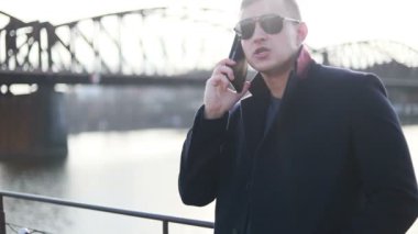 Genç yakışıklı işadamı cadde boyunca geri telefon yürüyüş İş görüşmesinde şık erkek takım elbise görünümüdür konuşuyor, cityscape arka plan üzerinde duruyor. Konsept: teknoloji, iş.