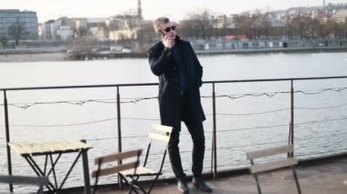 Genç yakışıklı işadamı cadde boyunca geri telefon yürüyüş İş görüşmesinde şık erkek takım elbise görünümüdür konuşuyor, cityscape arka plan üzerinde duruyor. Konsept: teknoloji, iş.