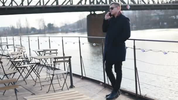 年轻的帅气商人在电话里走在大街上 后面的一条优雅的男人穿着西装 站在商业的话题上 站在城市风景的背景下 — 图库视频影像