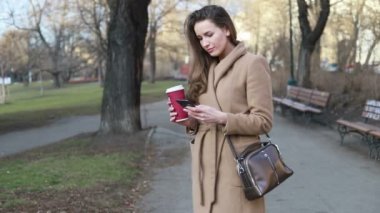 İçkiler ve insanlar konsepti - mutlu genç kadın ya da genç kız şehir bankında oturmuş kağıt bardaktan kahve içiyor.