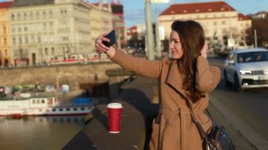 Bir kadın selfies bir şehirde yapma bir kağıt kahve Kupası ile önden görünümü. Sosyal medya kavramı. Gerçek zamanlı orta atış kilitli