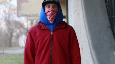 Kar maskeli, kimliği belirsiz genç adam duvarın yanında duruyor ve elinde sprey boya tutuyor. Vandalizm, sokak sanatı, hobi. Banliyö bölgesi, eğlence, isyan, protesto. Görüntüyü kapat