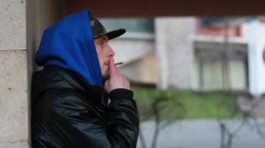 Portrait of stylish man smoking cigarette on urban background during sunset, slow motion, close up