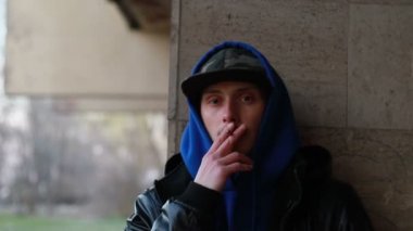 Portrait of stylish man smoking cigarette on urban background during sunset, slow motion, close up