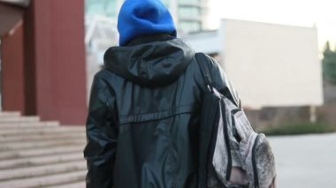 Genç adam yürüyor. Arkaya bakın. Bir sırt çantası ile arka genç turist adam yavaş hareket görünümü şehir gün güneş güneş ışığı etkinlik yürüyüş seyahat etmek sokak tatil yolculuk