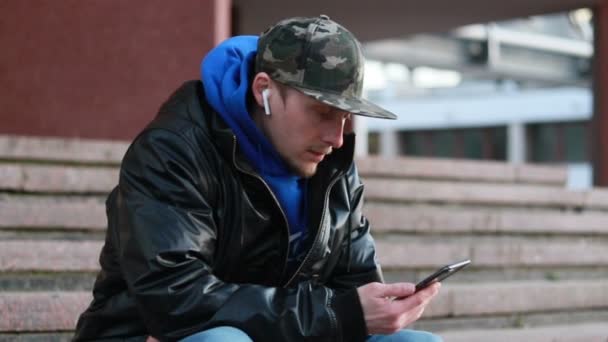 Jovem Bonitão Com Mochila Falar Telefone Com Auscultadores Sem Fios — Vídeo de Stock