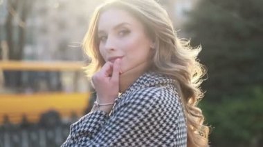 Bir şehirde sokakta bir ceket çekici kız, güneş parlıyor, kamera ve gülümsüyor döner daha. portre mutlu yavaş hareket yaz yüz günbatımı güzel bayan açık closeup sevimli