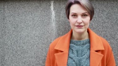 Portre genç çekici gülümseme kadın şehir merkezinde kamera bakmak mutlu moda kız yaz yüz teknoloji güneş güzel yavaş hareket sokak hissediyorum. şehirde turuncu bir ceket bir kız portresi