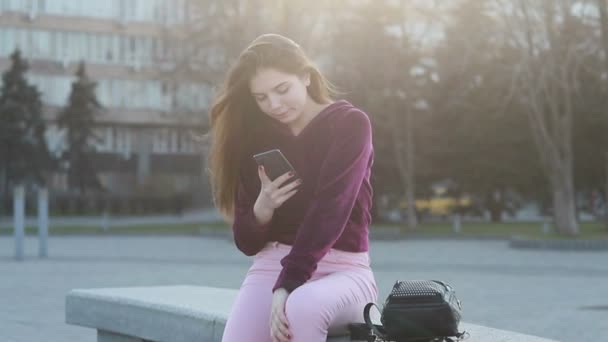 迷人的年轻女子漫步在阳光明媚的城市街道和朋友聊天 快乐的时髦女孩使用手机户外 日落背景 — 图库视频影像