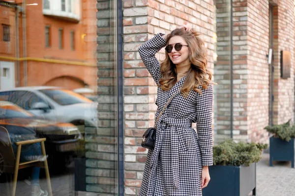 Aantrekkelijk meisje in een jas in de straat in een stad, zon schijnt — Stockfoto