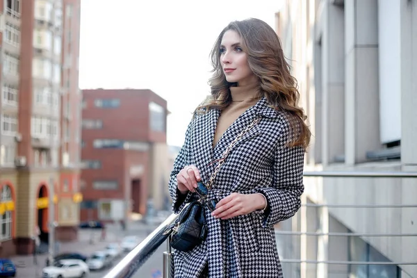 Aantrekkelijk meisje in een jas in de straat in een stad, zon schijnt — Stockfoto