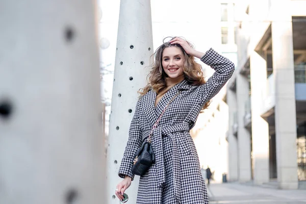 Chica atractiva en un abrigo en la calle en una ciudad, el sol está brillando — Foto de Stock