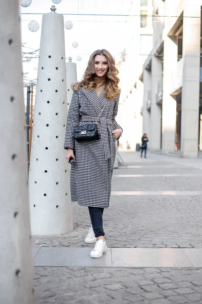Chica atractiva en un abrigo en la calle en una ciudad, el sol está brillando —  Fotos de Stock