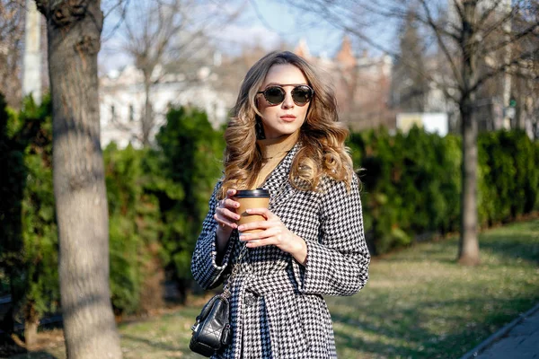 Mulher em casaco de trincheira andando e bebendo café de copo de papel — Fotografia de Stock