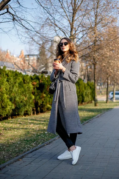 Mujer en gabardina caminando y bebiendo café de taza de papel — Foto de Stock