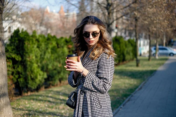 Mulher em casaco de trincheira andando e bebendo café de copo de papel — Fotografia de Stock
