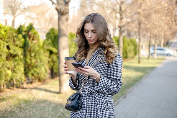 Mujer en gabardina caminando y bebiendo café de taza de papel — Foto de Stock