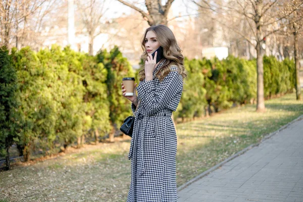 Mujer en gabardina caminando y bebiendo café de taza de papel — Foto de Stock