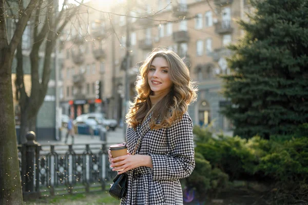 Mujer en gabardina caminando y bebiendo café de taza de papel — Foto de Stock